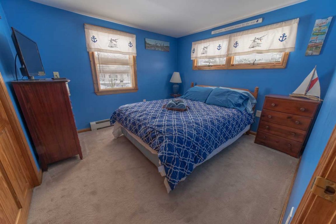 A blue-painted bedroom with a bed, dresser, nightstand, and TV.