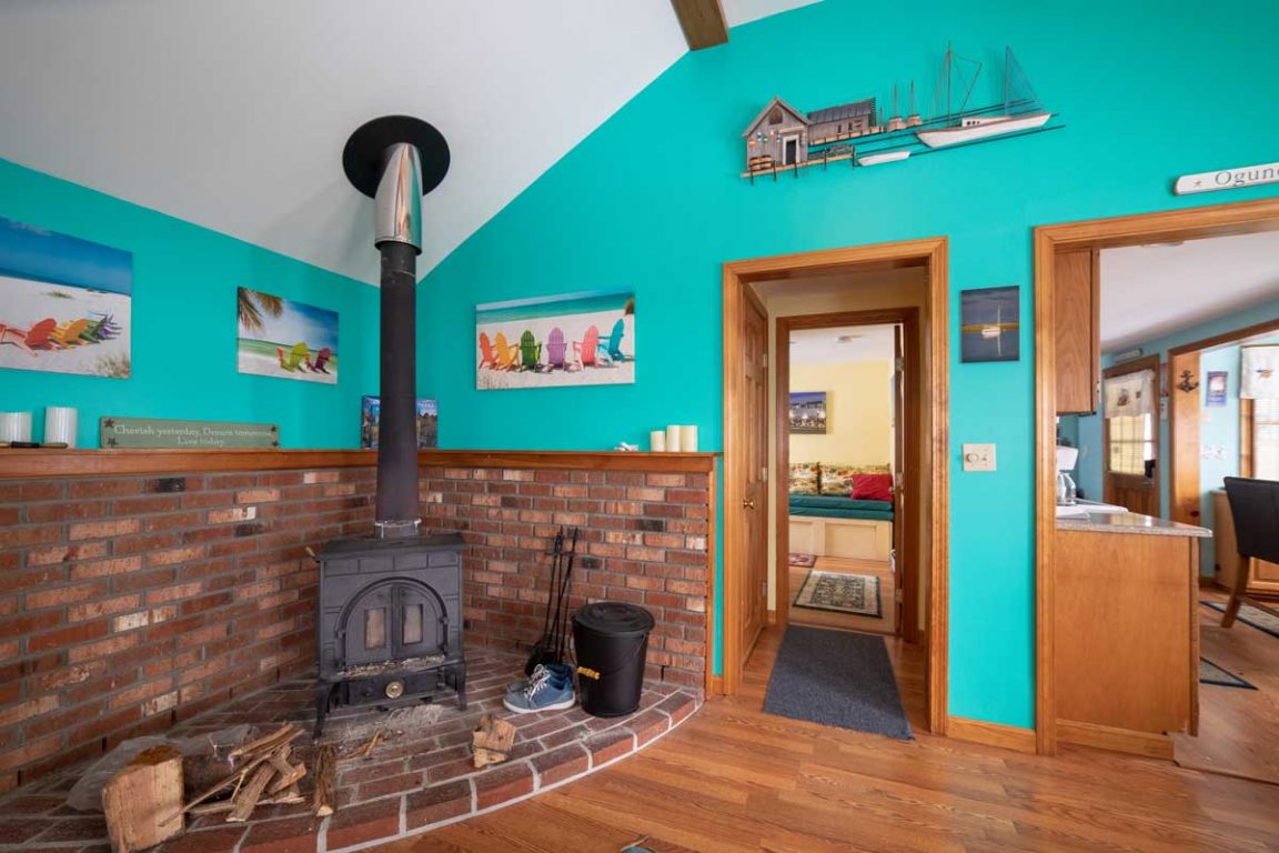 A cozy living area with a brick fireplace, vaulted ceiling, and open doorway.