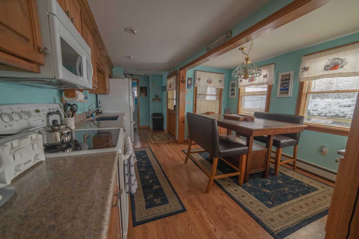 A kitchen with a dining area, featuring a small kitchenette with a microwave, stove, and sink, and a dining table with four chairs.