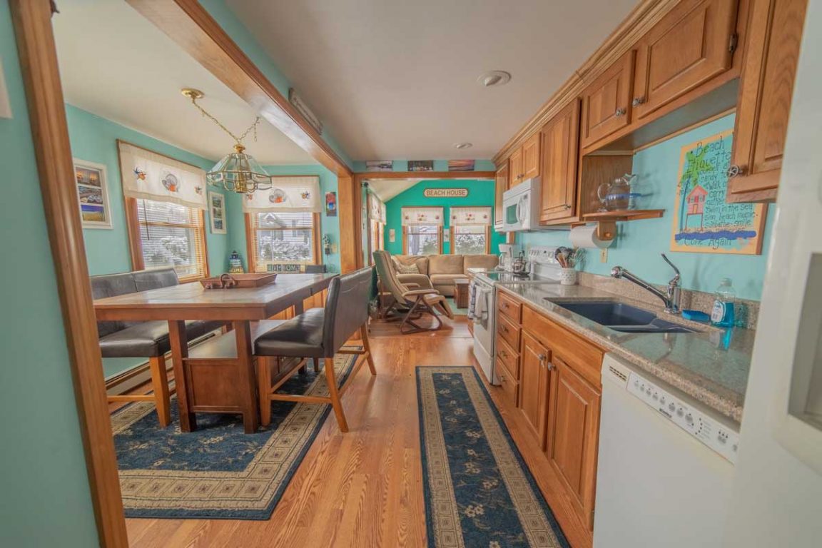 A wide view of a kitchen and dining area with wooden cabinets, granite countertops, and a dining table with chairs.