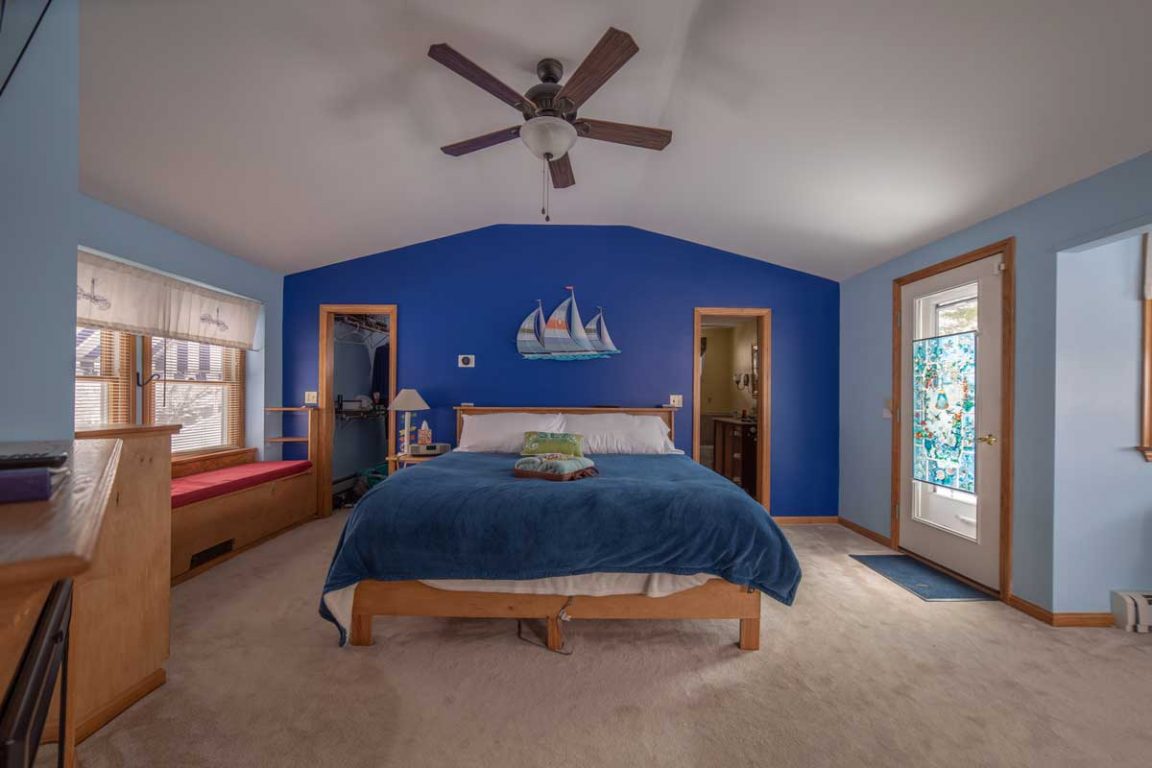 A wide view of a bedroom with a blue accent wall, a wooden bed frame, and a ceiling fan.