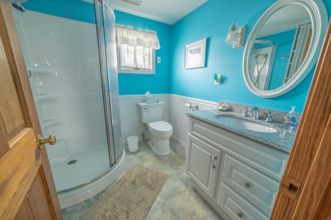 A bathroom with a curved shower, white vanity with granite countertop, and blue walls.